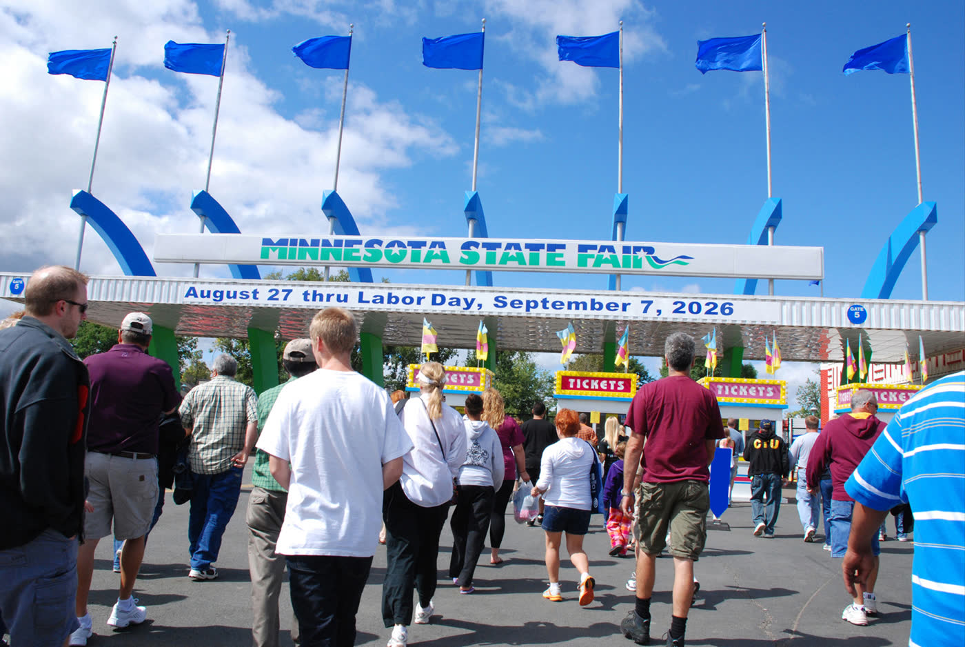 Main gate of the 2026 Minnesota State Fair, dates on the banner, crowd approaching from a distance.